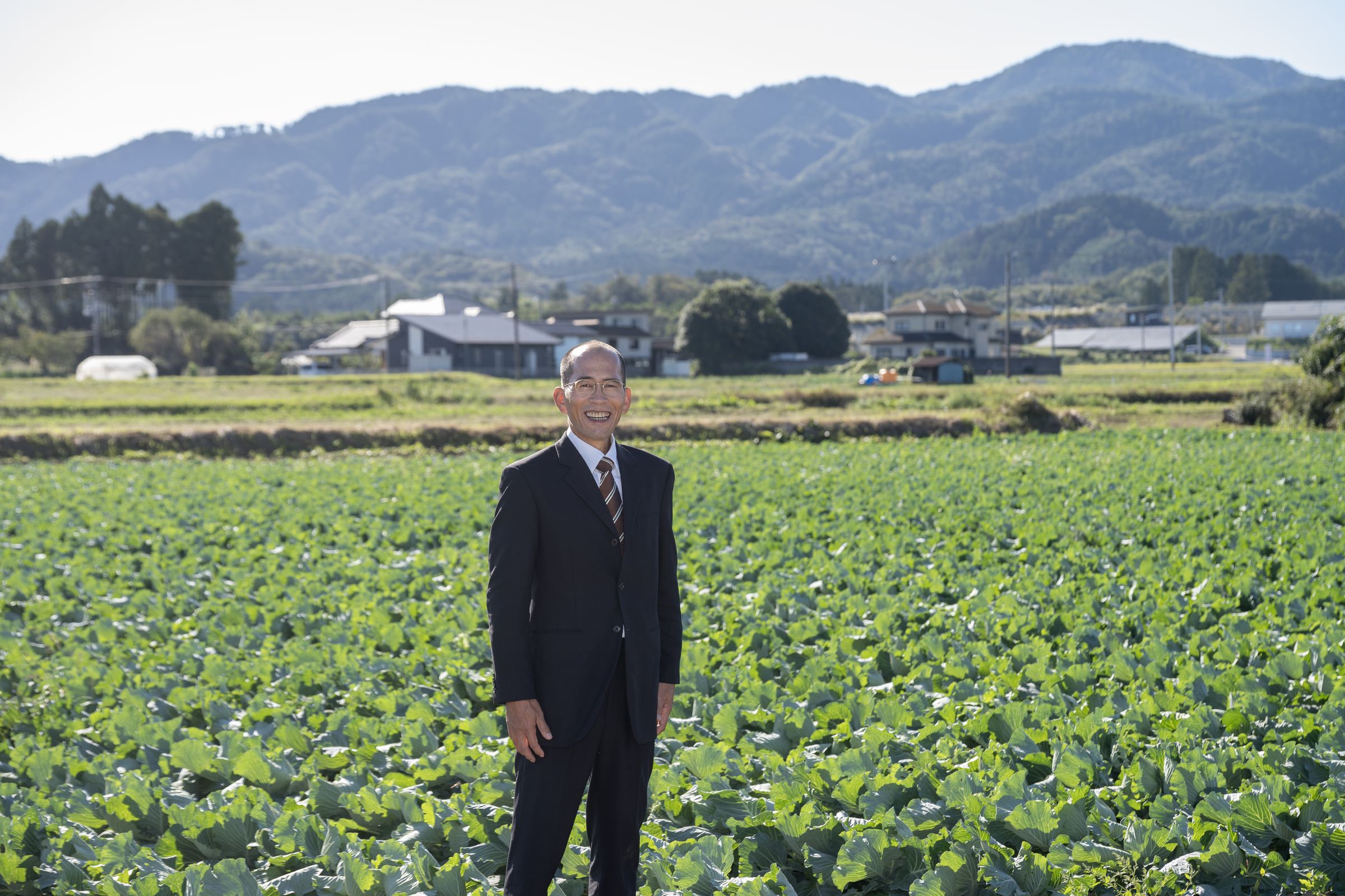 山並みと畑を背に立つ豊田まさお