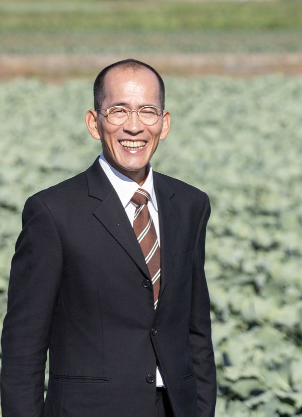 畑を背に笑顔の豊田まさお